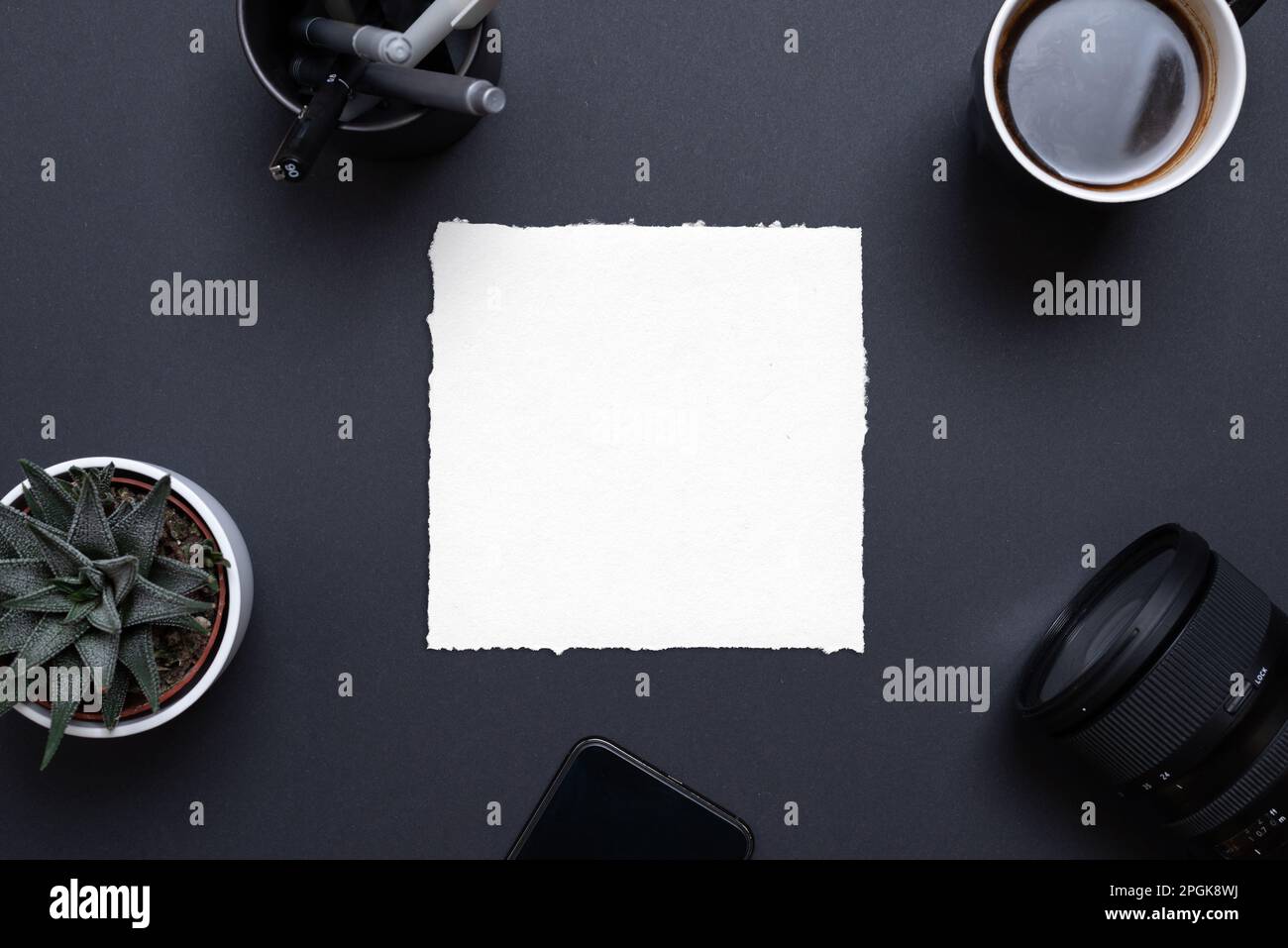 Blank paper frame on black office desk surrounded by phone, camera, coffee mug, plant and pens. Top view, flat lay composition for copy presentation Stock Photo