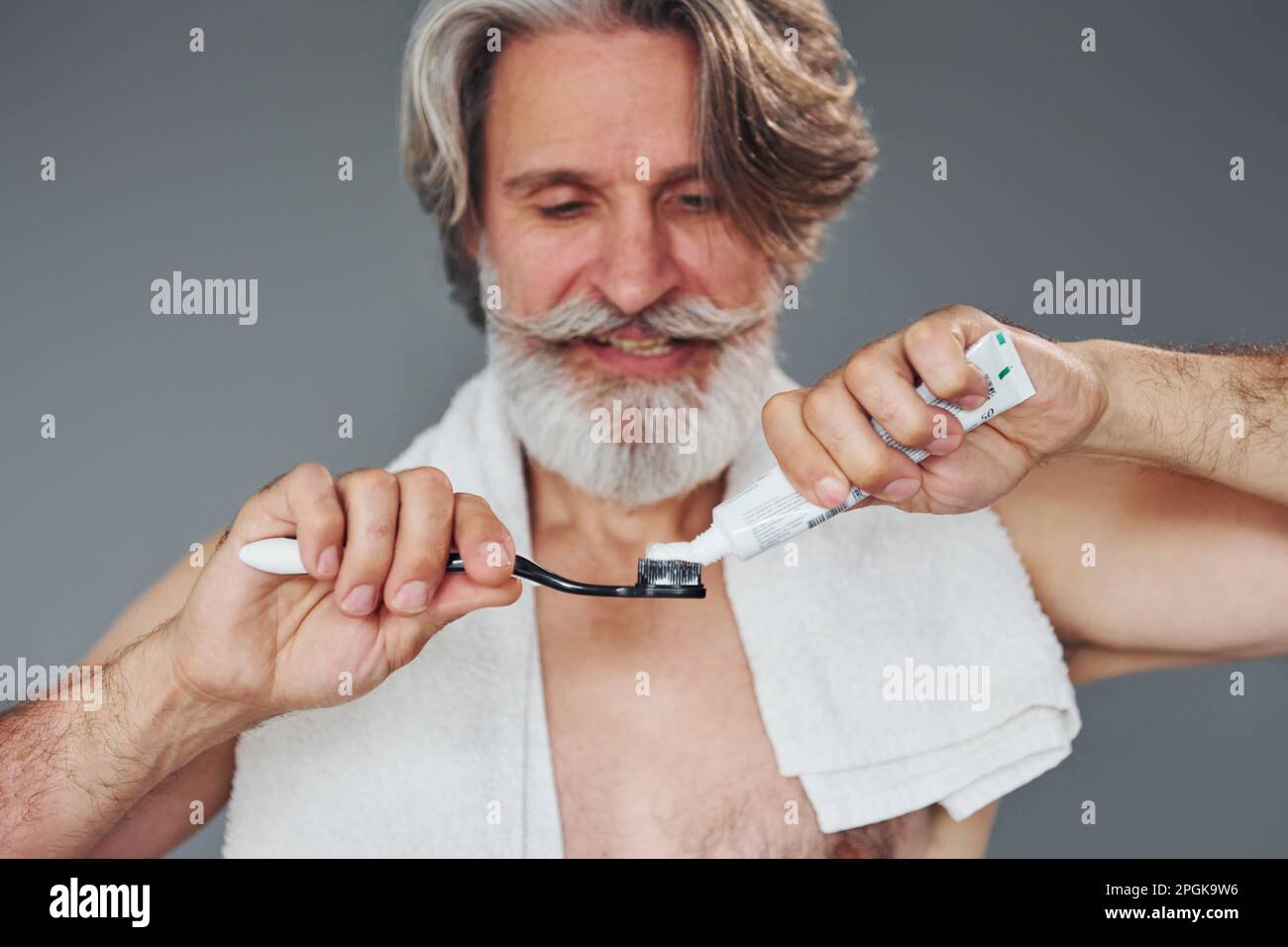 Using toothpaste. Stylish modern senior man with gray hair and beard is