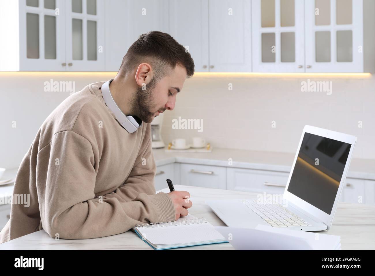 Young man using modern laptop for studying in kitchen. Distance learning Stock Photo