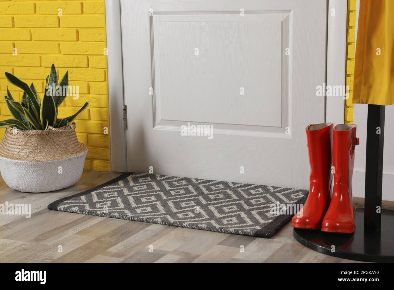 Hallway interior with beautiful houseplant, hanger stand and door mat on floor near entrance Stock Photo