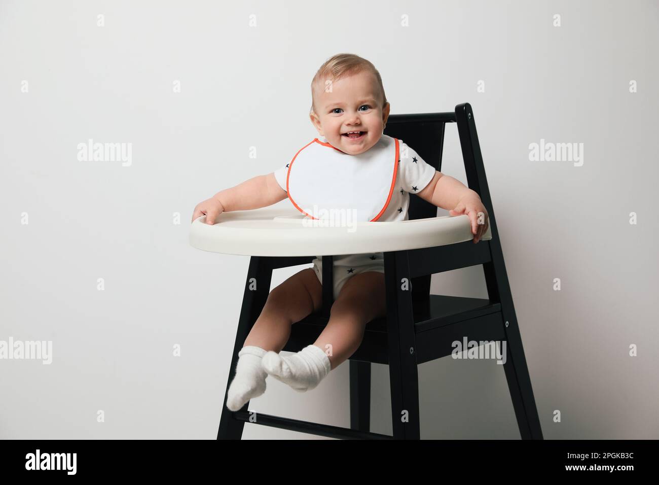 Cute little baby wearing bib in highchair on white background Stock