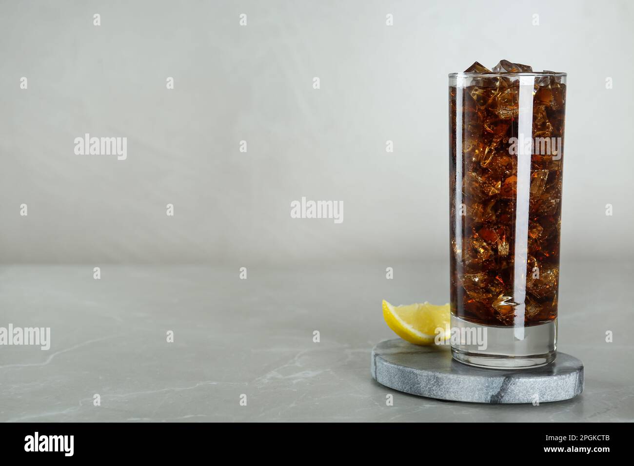 Glass of refreshing soda water with ice cubes and lemon on light grey ...