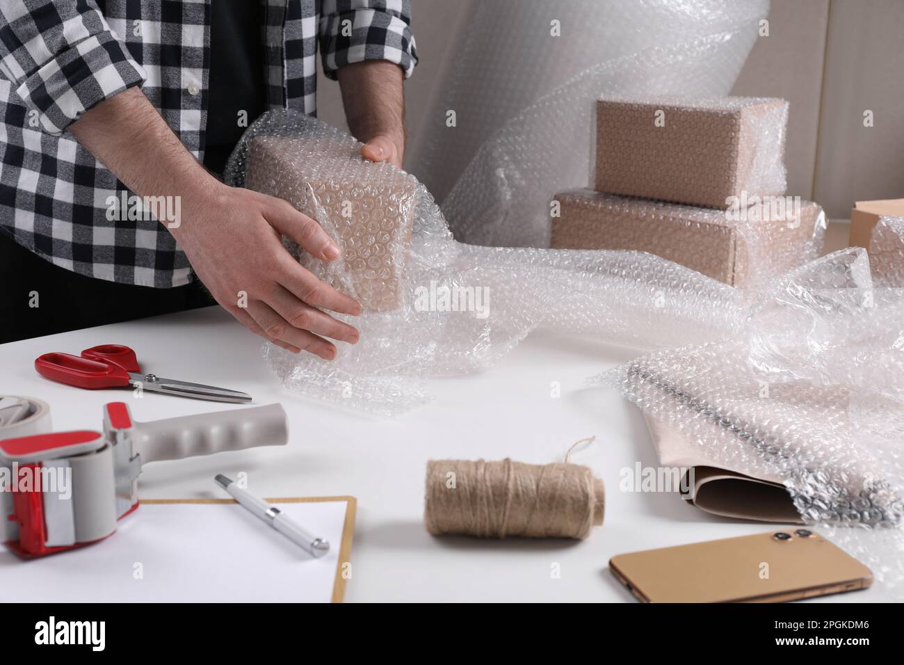 Man covering box with bubble wrap at table in warehouse, closeup Stock