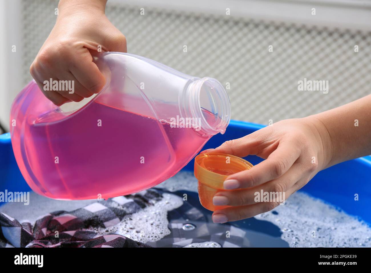 Woman pouring detergent into cap over basin with clothing, closeup