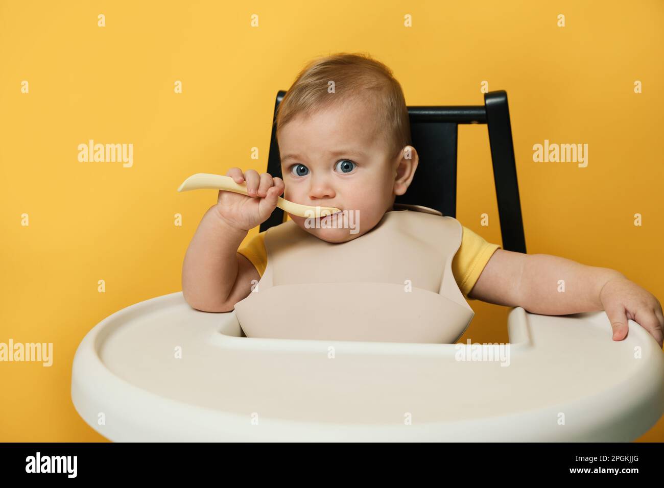 Cute little baby wearing bib while eating on yellow background Stock ...