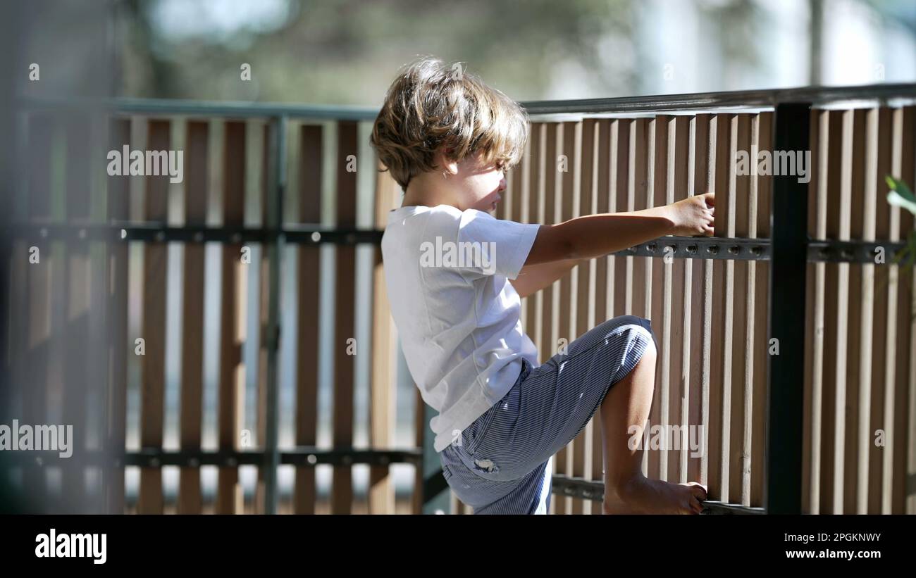 Child holding into balcony wooden fence at apartment residential building. Concept of security and protection of little boy at terrace Stock Photo