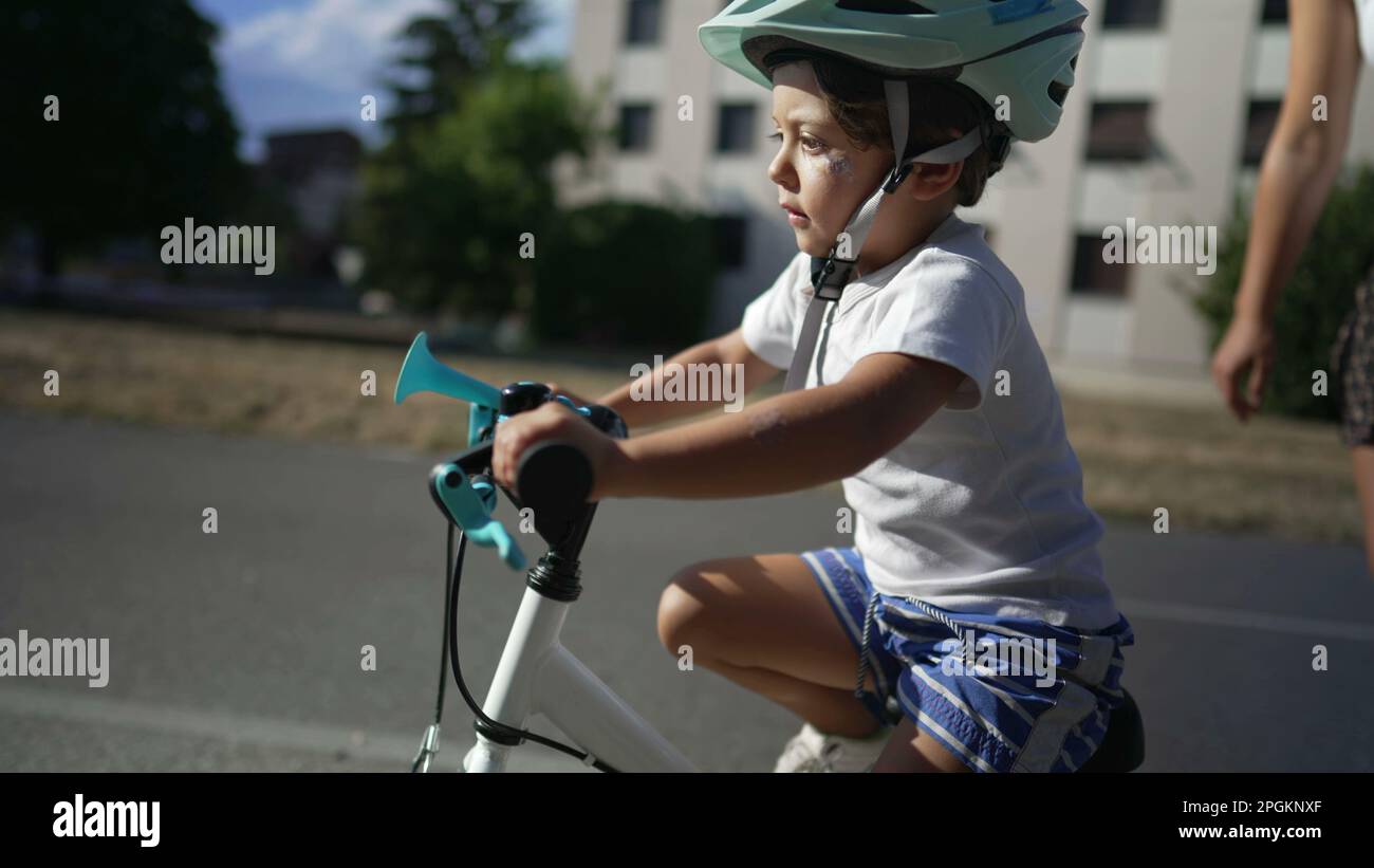 Child learns to ride bicyle wearing helmet outside with mother