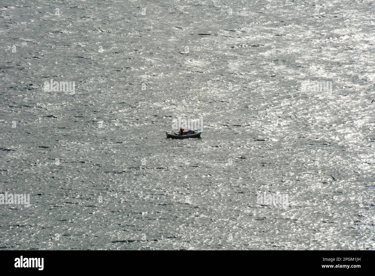A lone traditional fisherman fishing in a rowboat in the Strait of Bosphorus off the coast of Istanbul, Turkey / Turkiye. Stock Photo