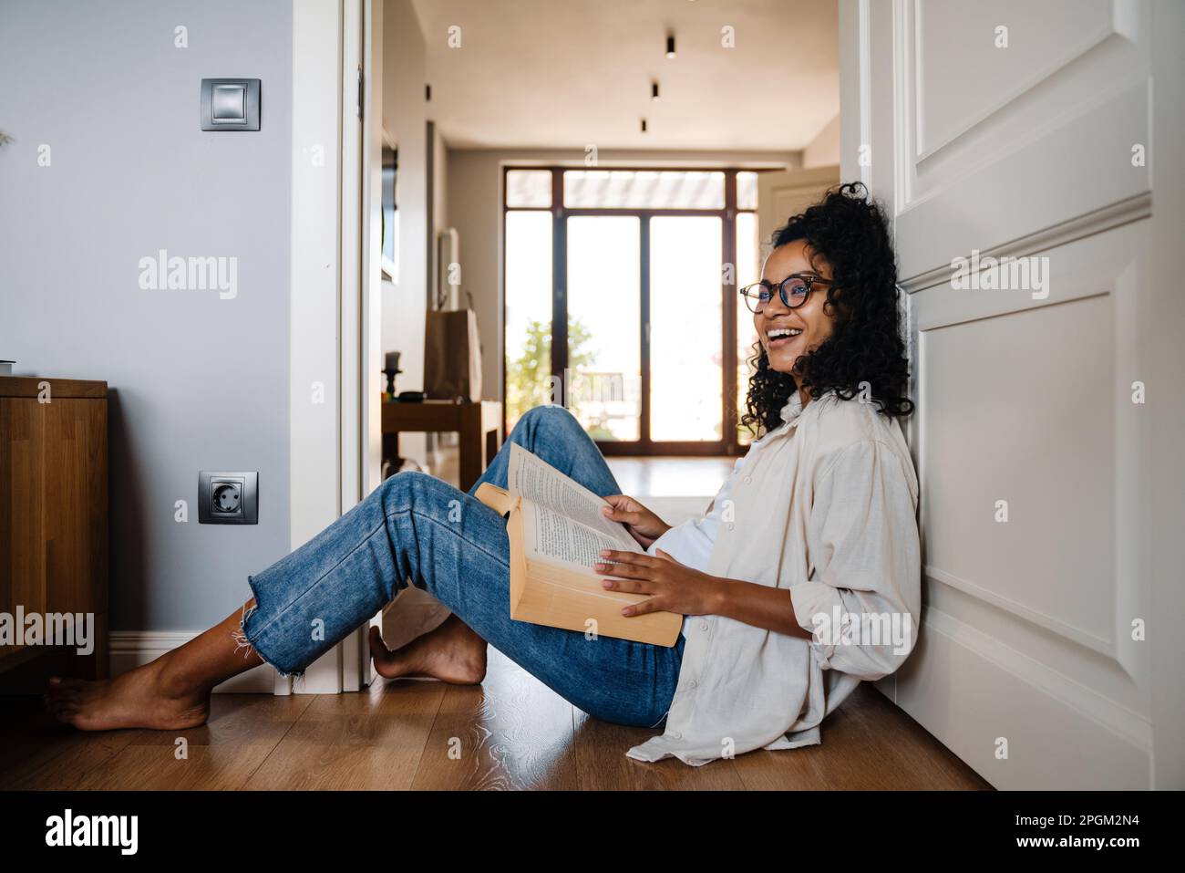 African american young woman with curly afro hairstyle sitting on floor at home and reading book Stock Photo