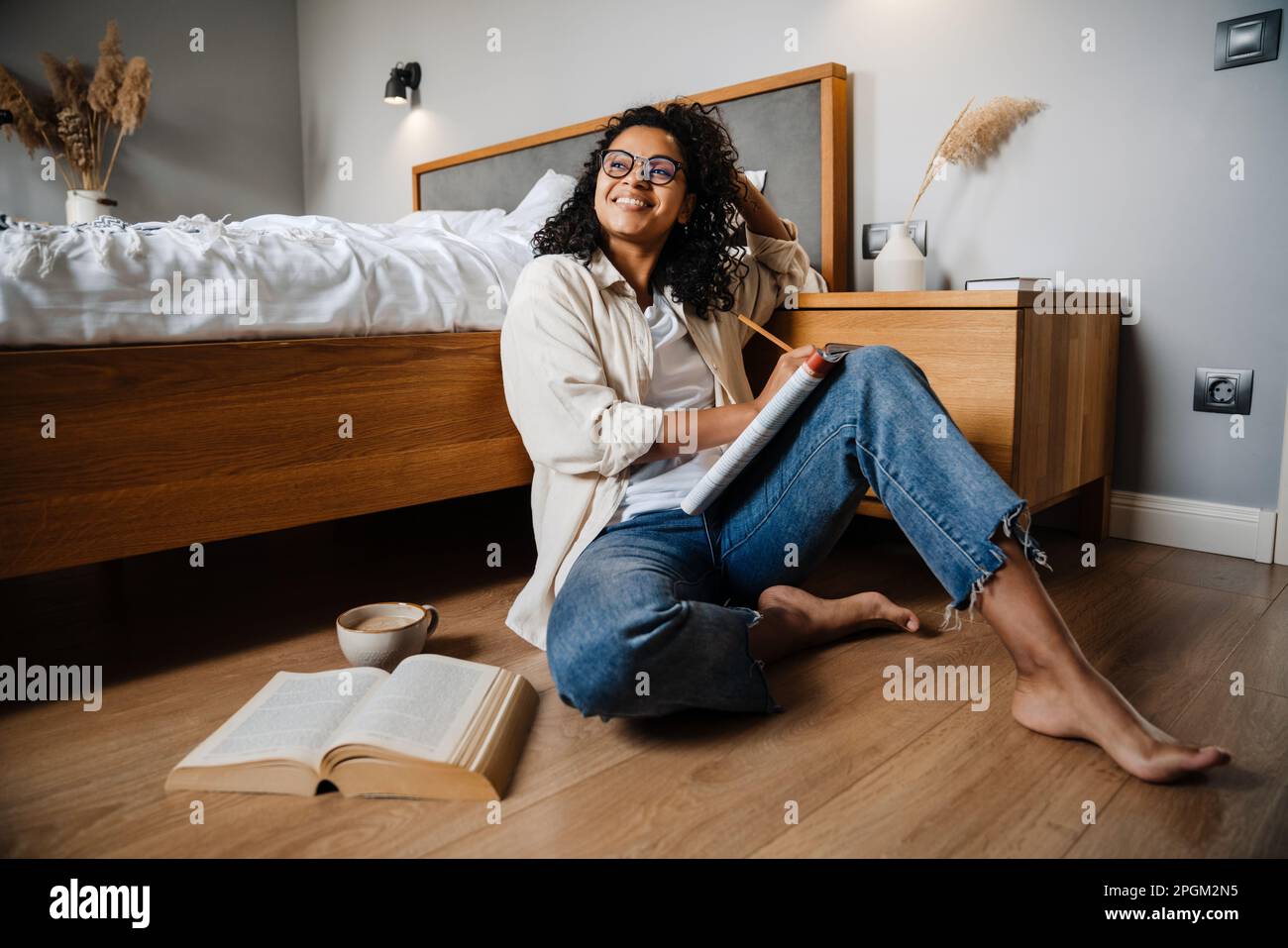 African american young woman sitting on floor at home and studying with exercise book Stock Photo