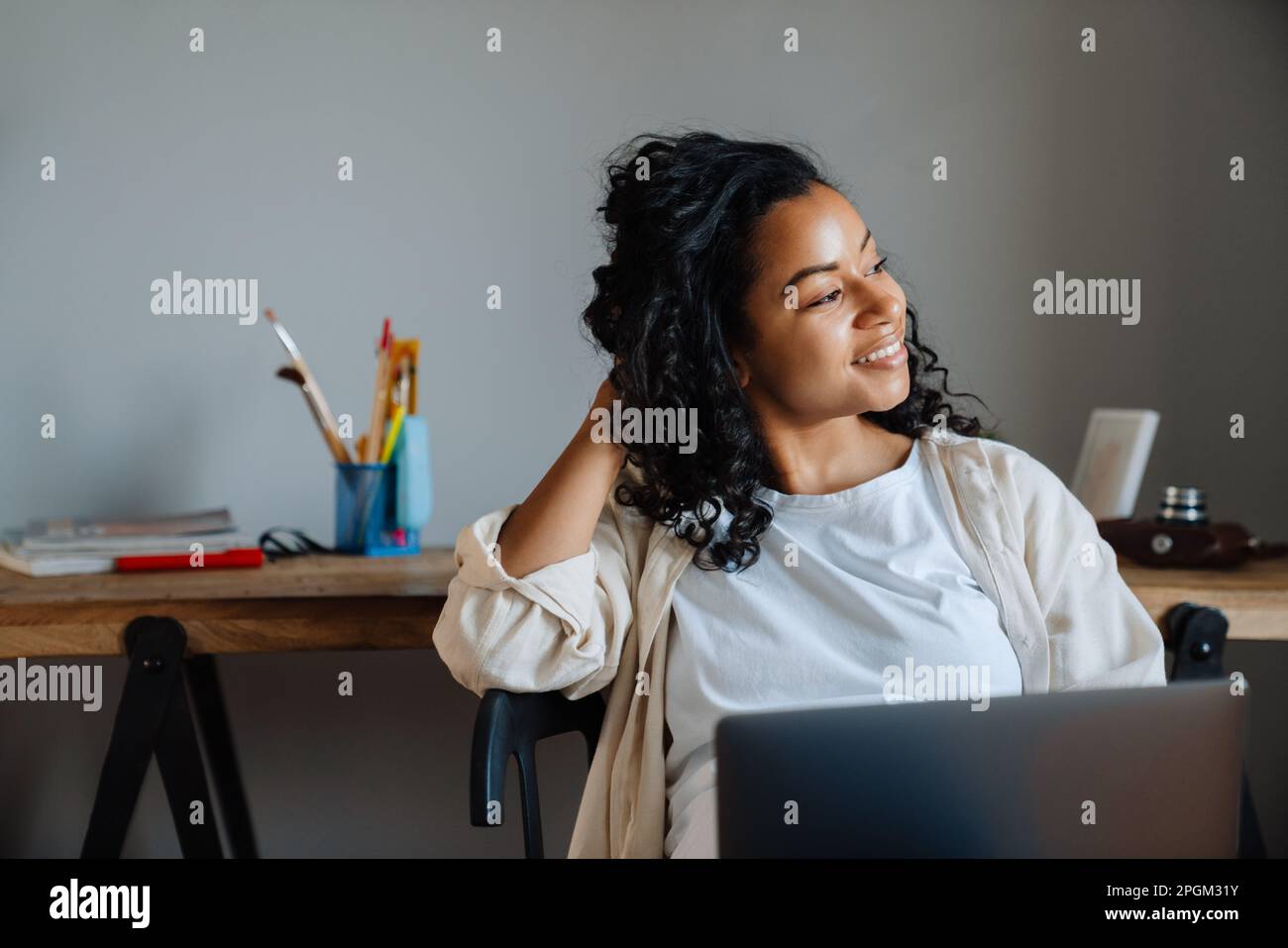 African american young woman with curly afro hairstyle sitting in chair and using laptop at home Stock Photo