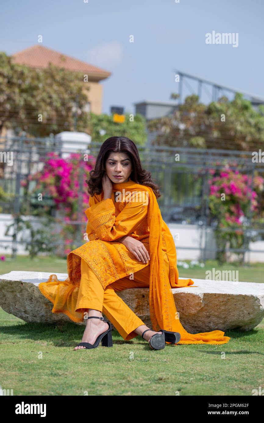 Female model posing outdoors wearing orange  Indian Pakistani Asian traditional salwar kameez, Stock Photo