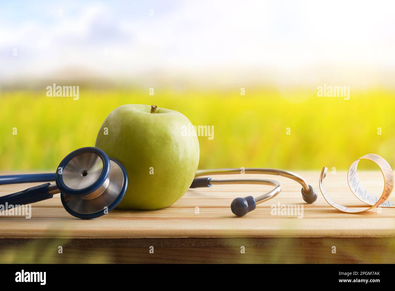 Health and check up concept with apple and stethoscope and tape measure around on wooden table with nature background. Front view. Stock Photo