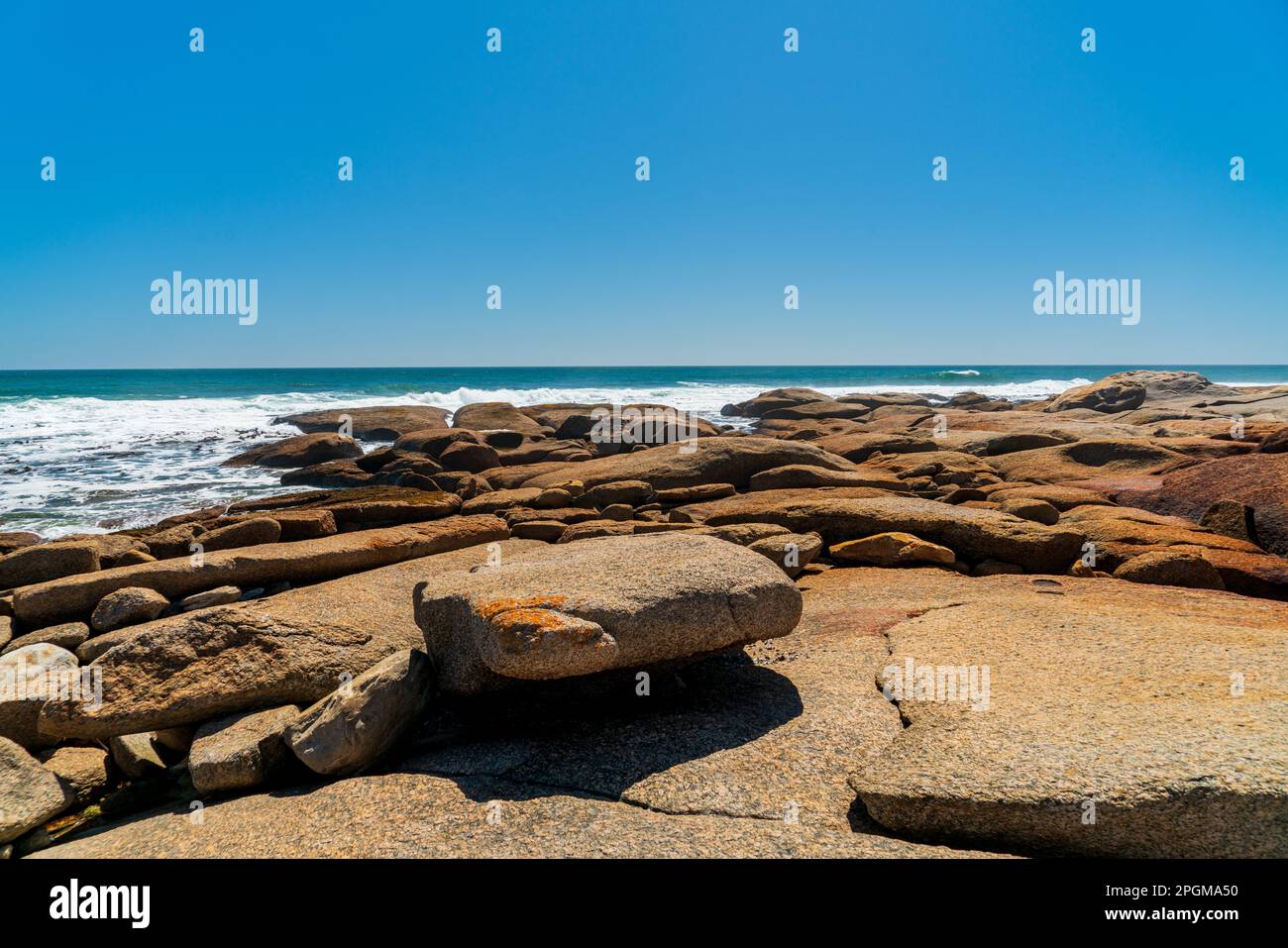 Tranquil sea shore in South Africa,  with big red rocks on a sunny day with blue sky. Stock Photo