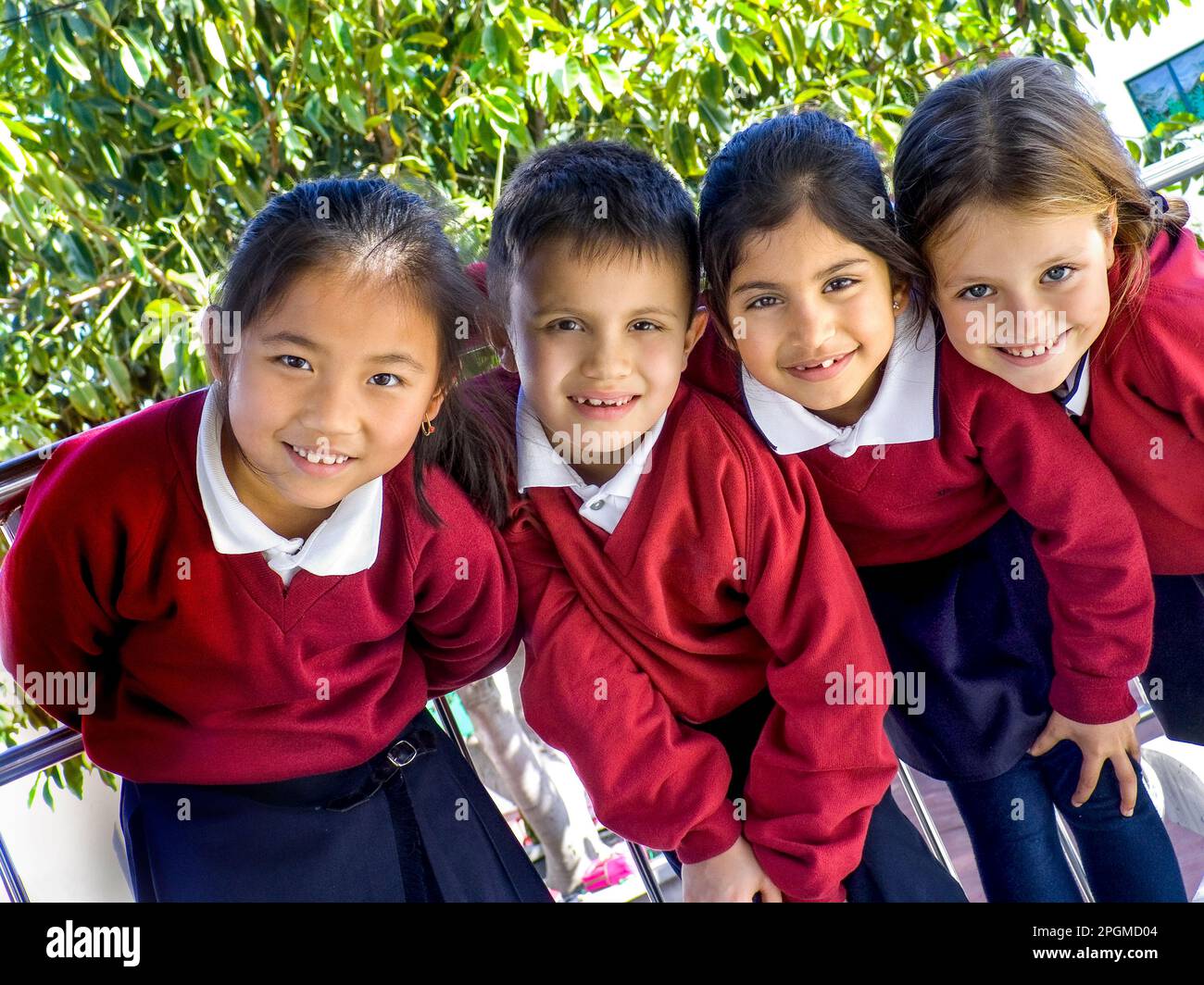 Multicultural Infant Young Junior school children in uniform outside in sunny playground. Korean, Hispanic, Asian and Cauacasian school pupils pose together in sunny clean spacious educational environment  Junior School Pupils 5-9yrs  Fun Happy group of young junior mixed race junior school children smile to camera at playtime outside in sunny playground Stock Photo