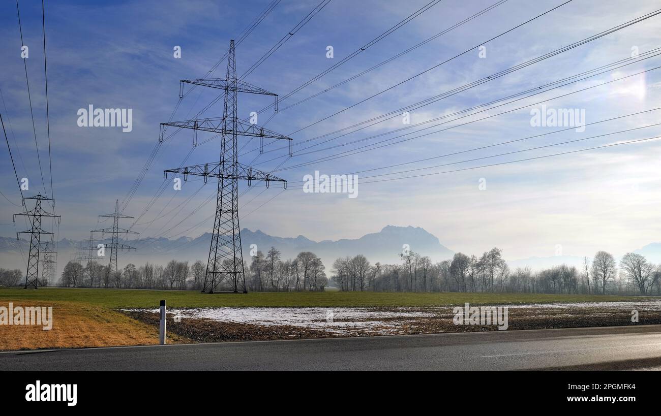 Landscape in winter behind road with many power pylons in background ...