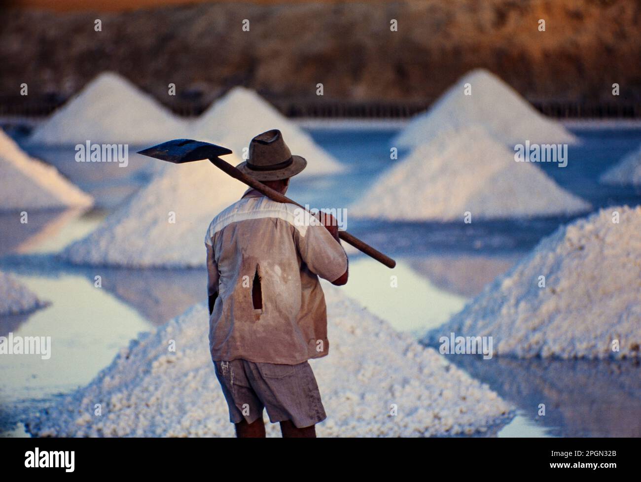 Salt mounds, elderly man works at sea salt harvesting, produced by the evaporation of seawater. Due to its semi-arid climate in the north coast, Rio Grande do Norte is responsible for producing over 95% of the Brazilian salt. Stock Photo