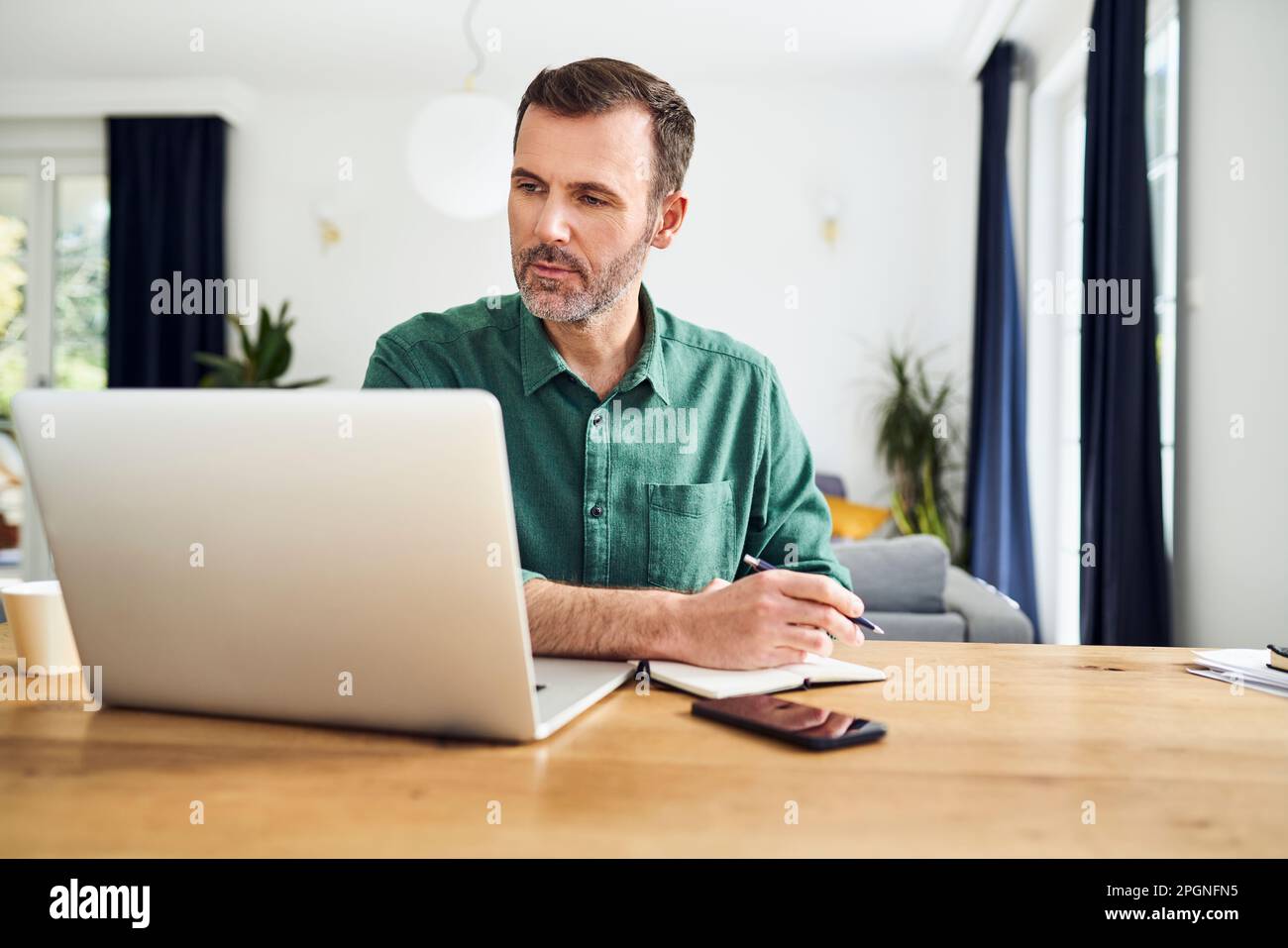 Handsome man working from home taking notes at desk Stock Photo