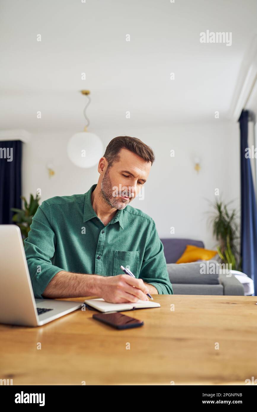 Handsome man working from home taking notes at desk Stock Photo