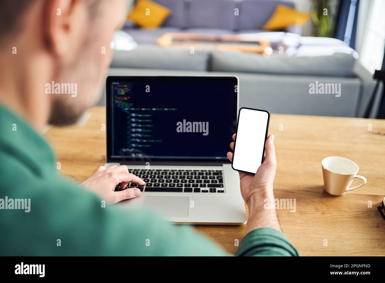 Man working on laptop at home holding phone with blank screen Stock Photo