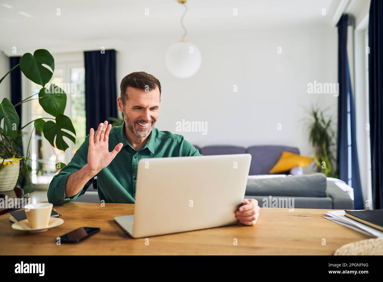 Cheerful man making video call waving at laptop Stock Photo