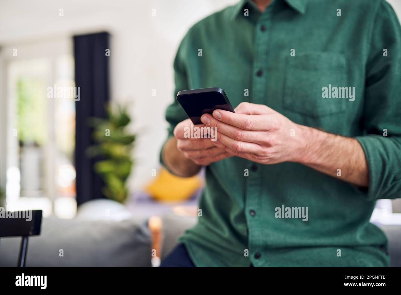 Man using smartphone leaning on couch Stock Photo