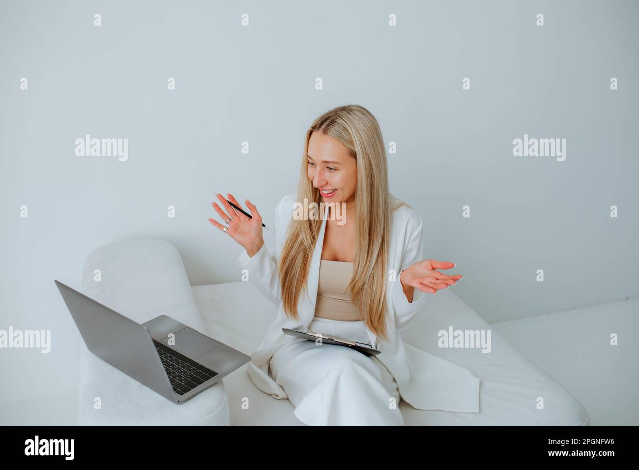 Happy psychologist gesturing through laptop sitting on couch in office Stock Photo