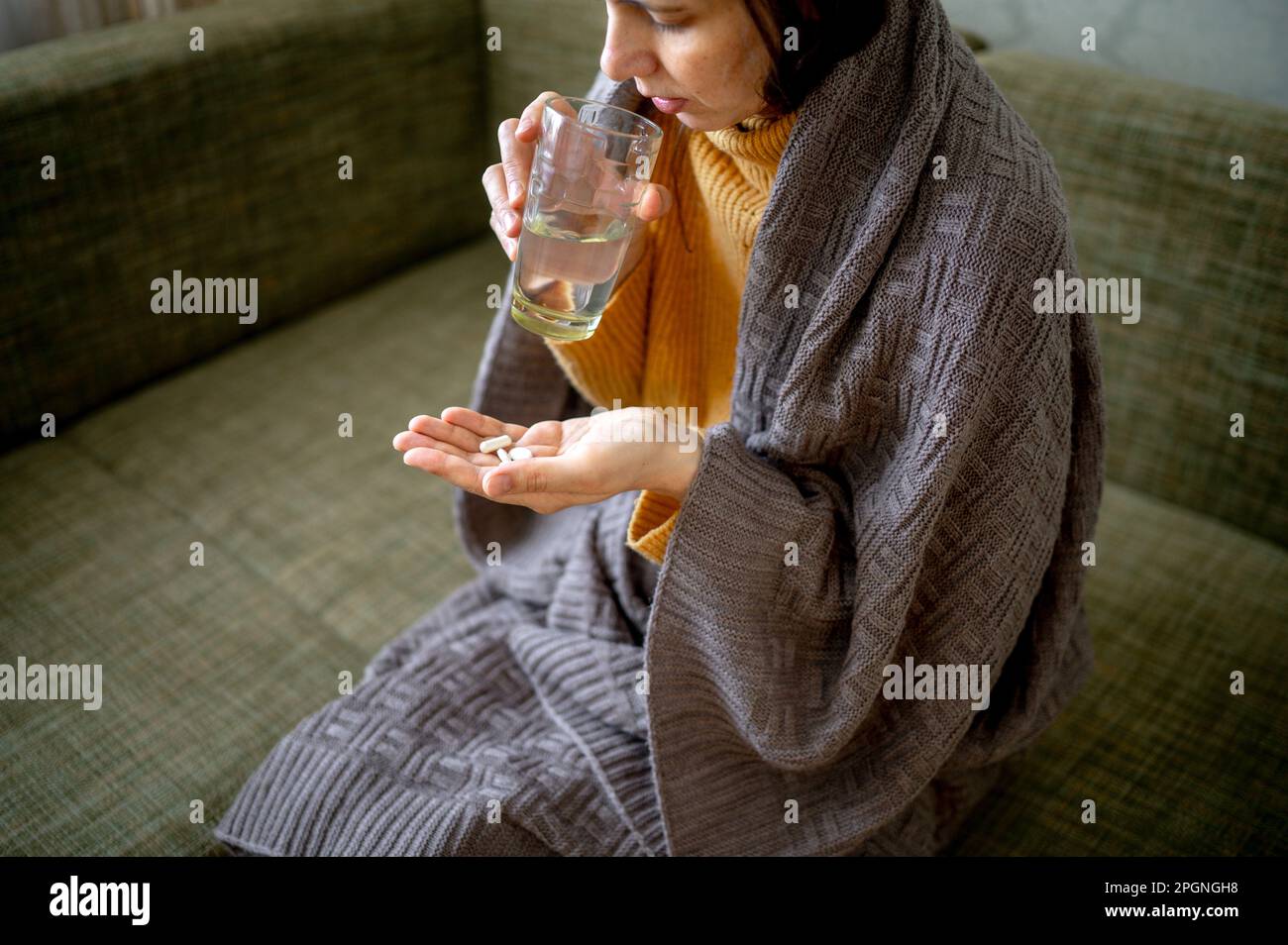Sick woman wrapped in blanket taking medicine at home Stock Photo