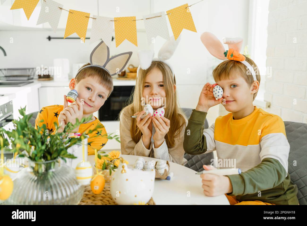 Happy boys and girl wearing rabbit ears headbands and holding Easter eggs at home Stock Photo