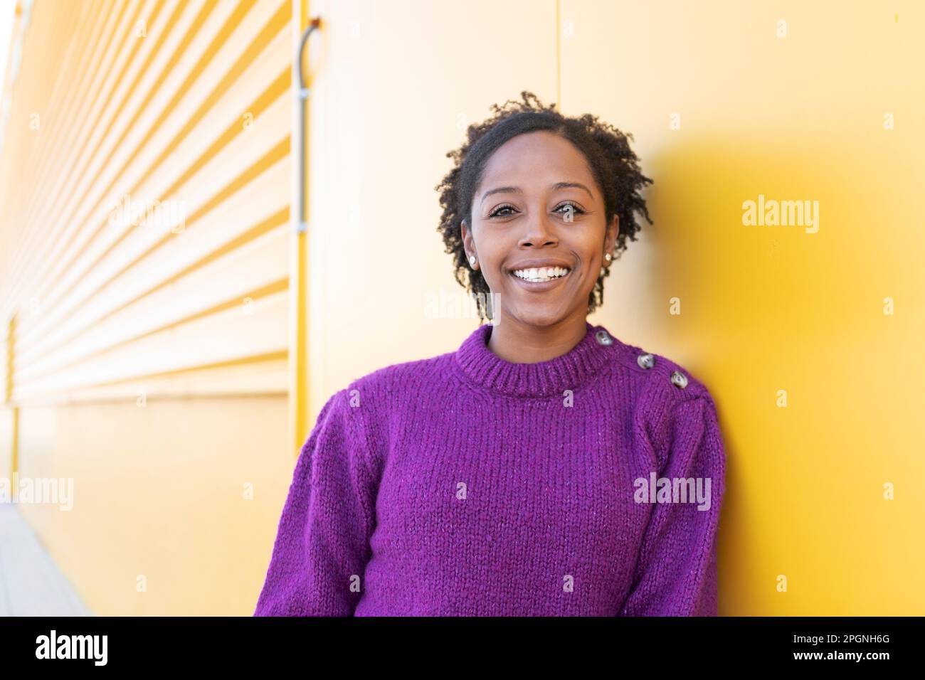 Happy woman wearing sweater standing by yellow wall Stock Photo