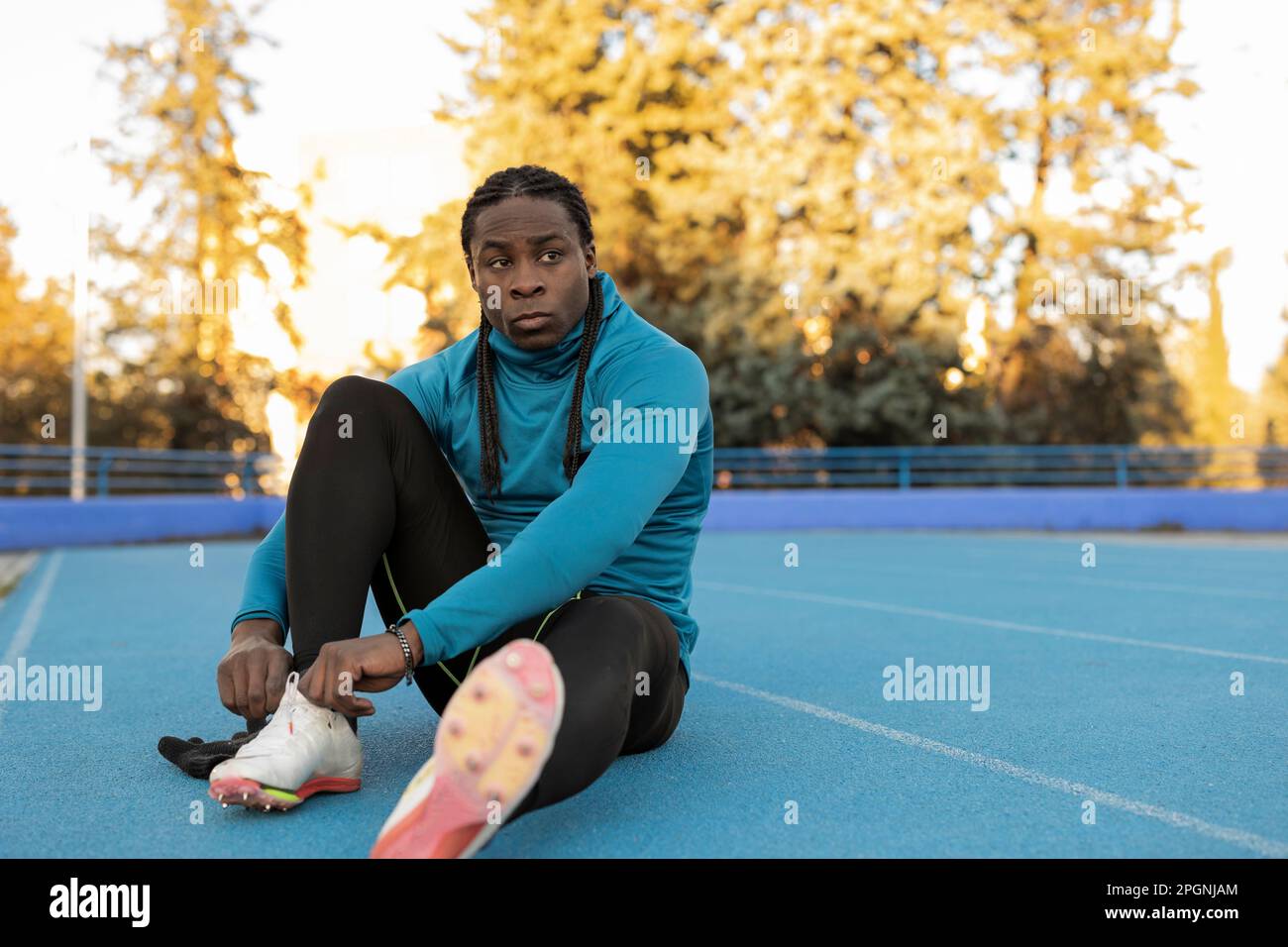 Thoughtful athlete tying shoelace sitting on sports track Stock Photo