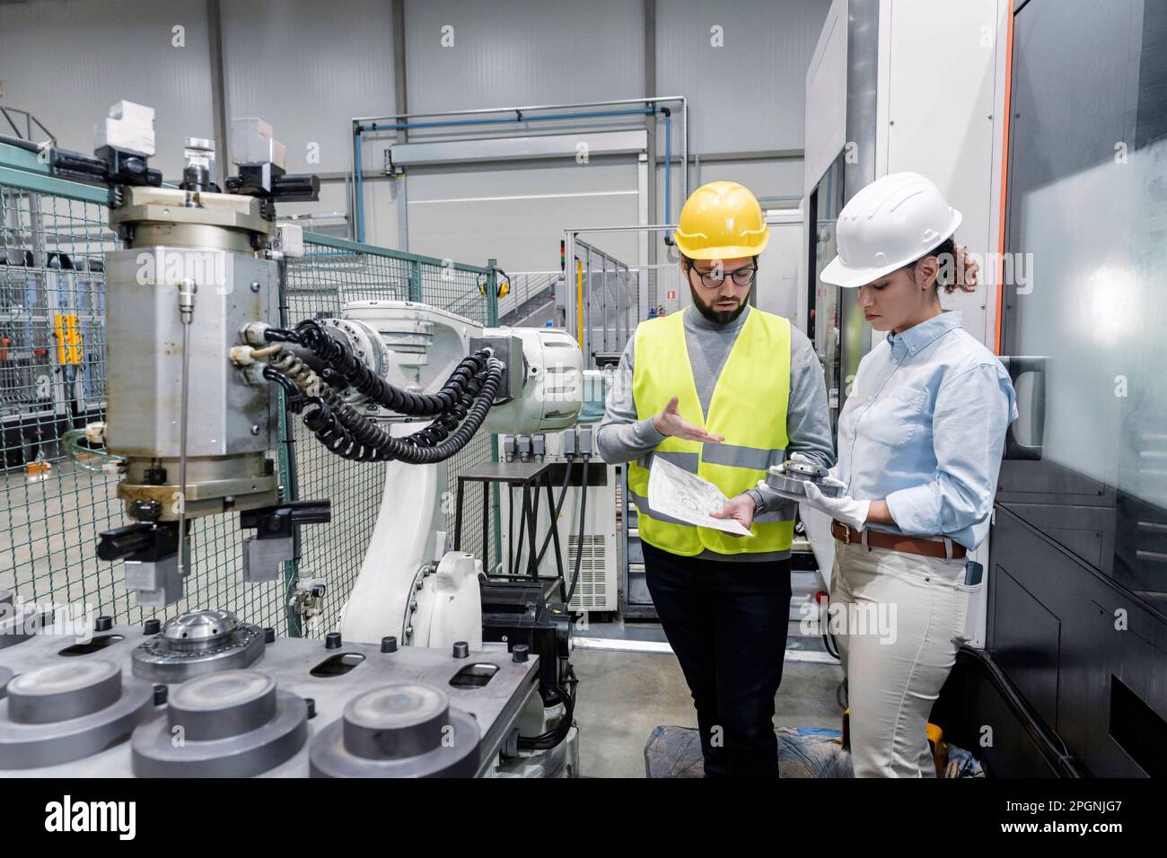 Young engineer explaining colleague with machine part in factory Stock Photo