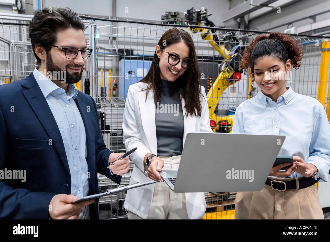 Happy businesswoman sharing laptop with colleague in factory Stock Photo