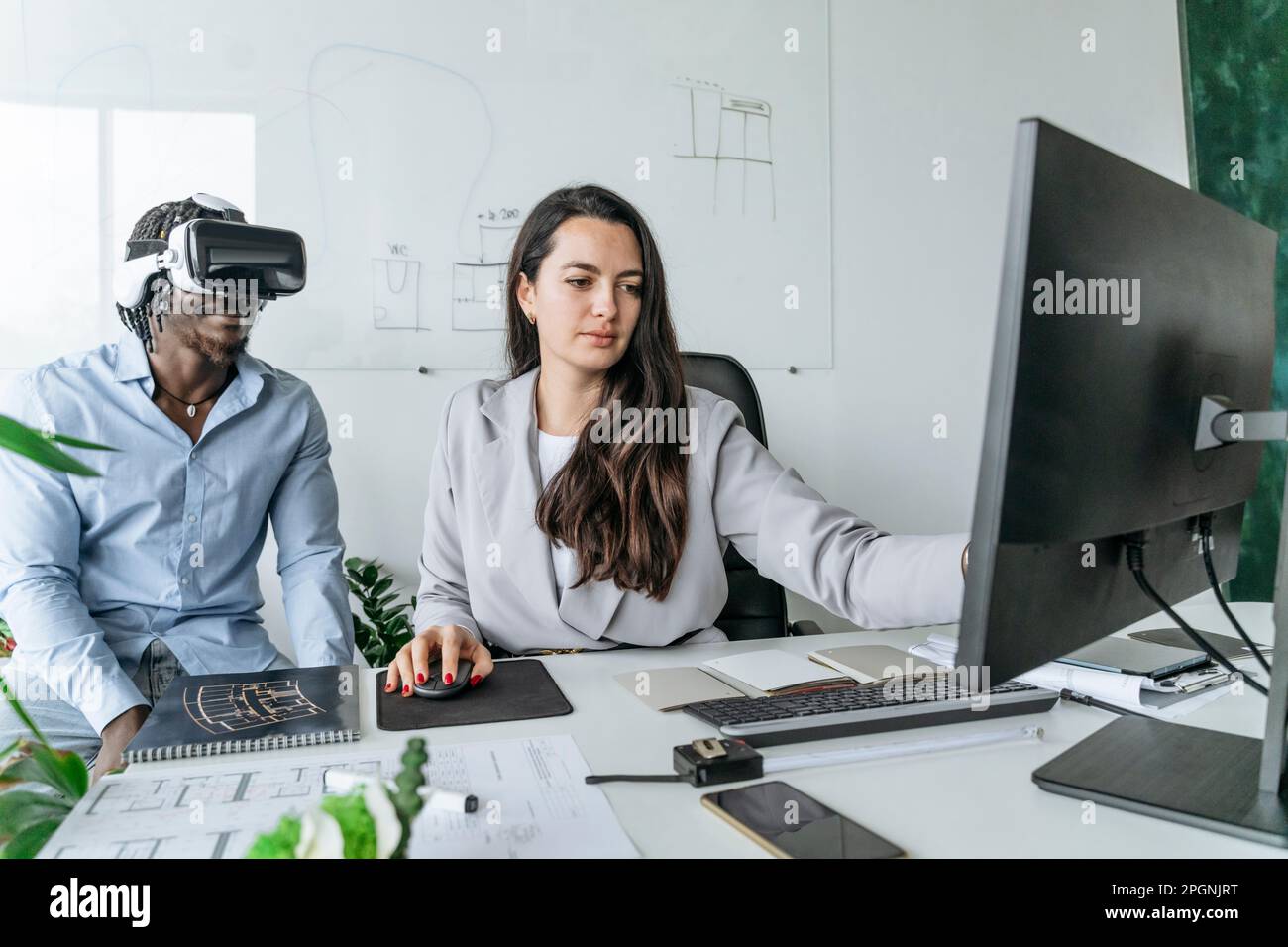 Architect using computer with colleague wearing virtual reality headset at office Stock Photo