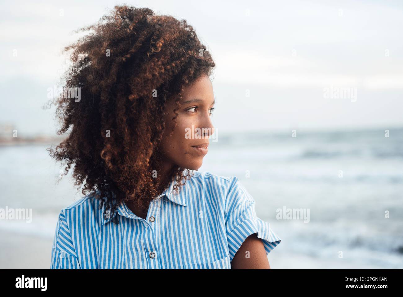 Contemplative young woman with curly hair in front of sea Stock Photo ...