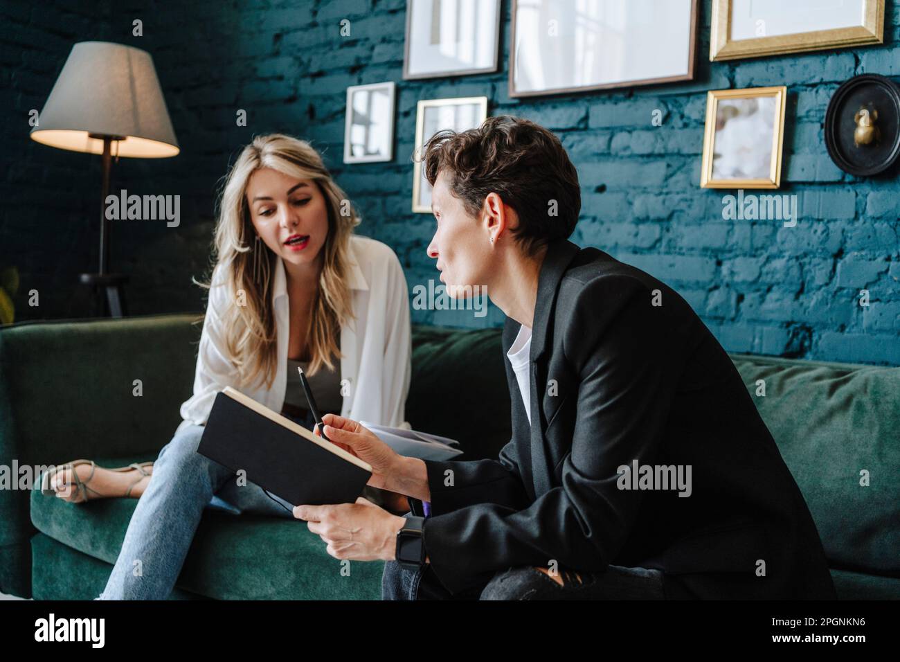 Producer holding book talking to actress sitting on sofa at film set Stock Photo