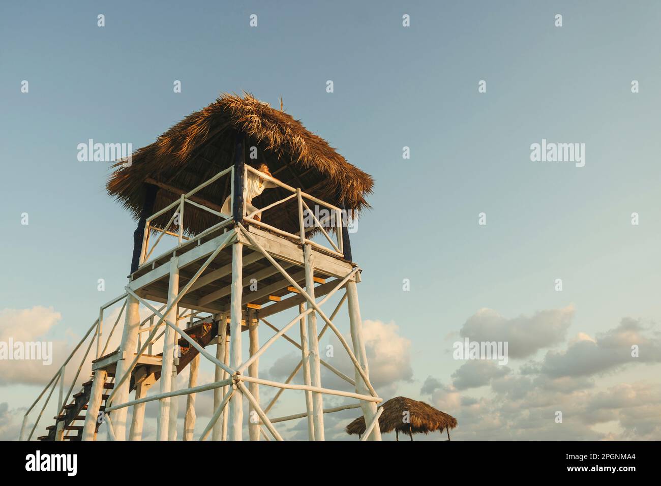 Woman spending leisure time at stilt house under cloudy sky Stock Photo