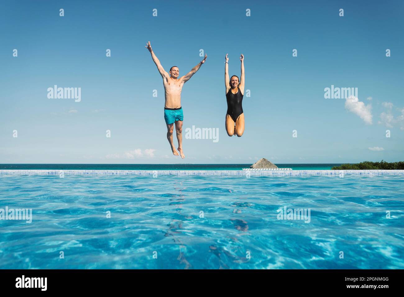 Carefree couple with arms raised jumping in swimming pool Stock Photo