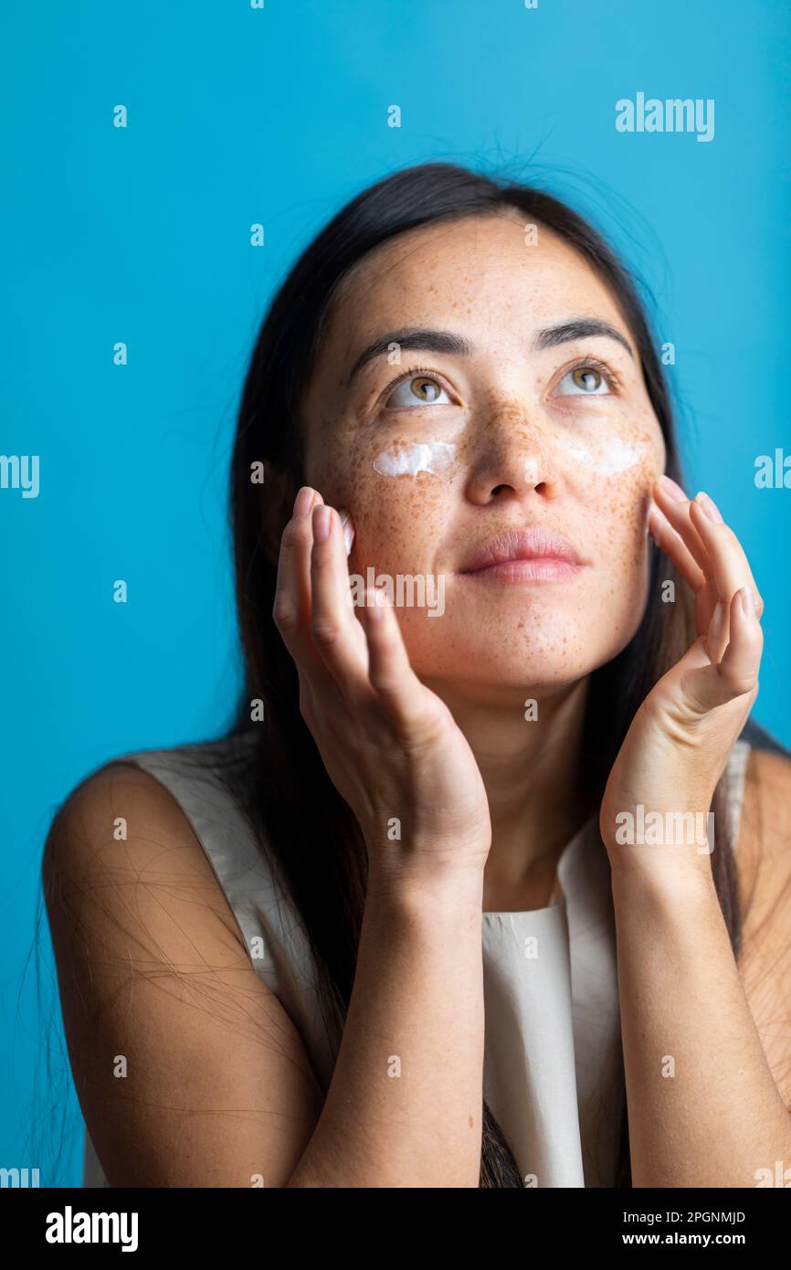 Woman applying cream on face against colored background Stock Photo