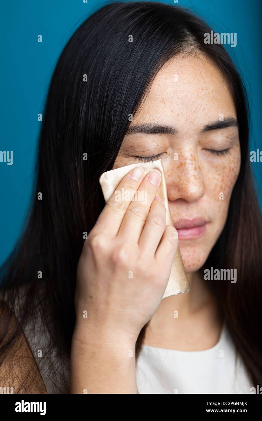Woman with eyes closed cleaning face against blue background Stock