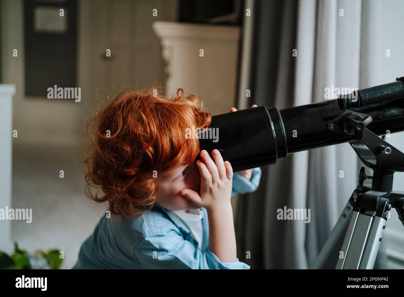 Redhead boy looking through telescope at home Stock Photo