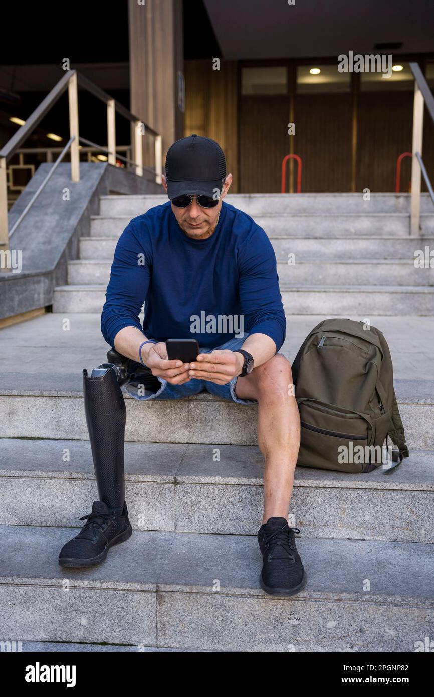 Mature man with disability using smart phone sitting on steps Stock Photo