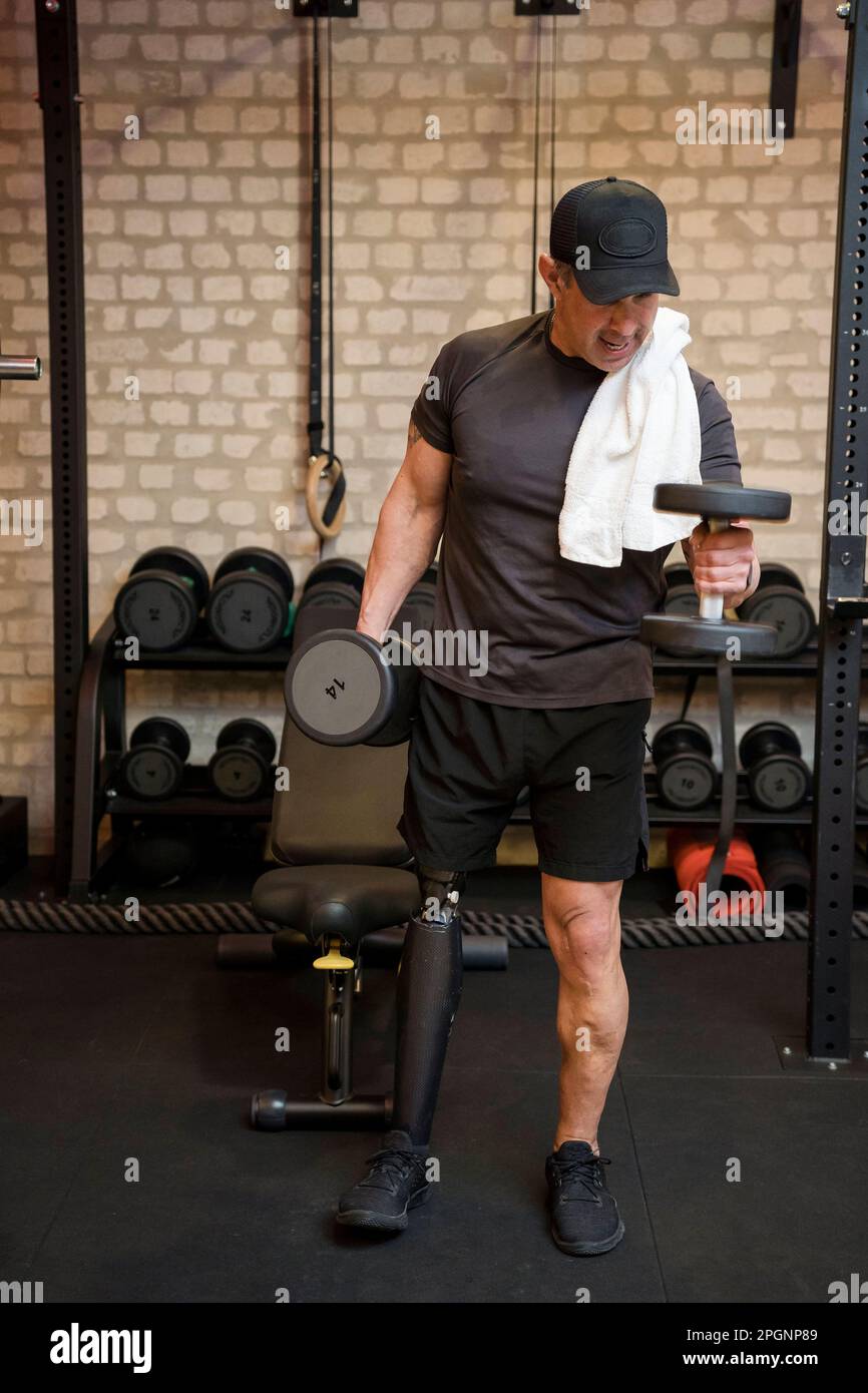 Mature man with prosthetic leg exercising with dumbbell in gym Stock Photo