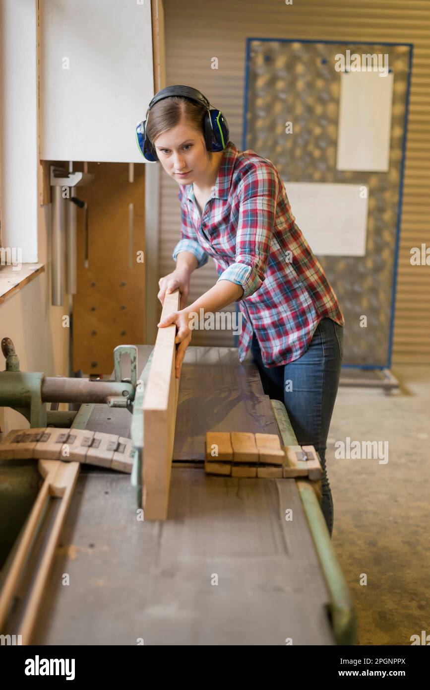 Craftswoman wearing ear protectors cutting wood in Stock Photo