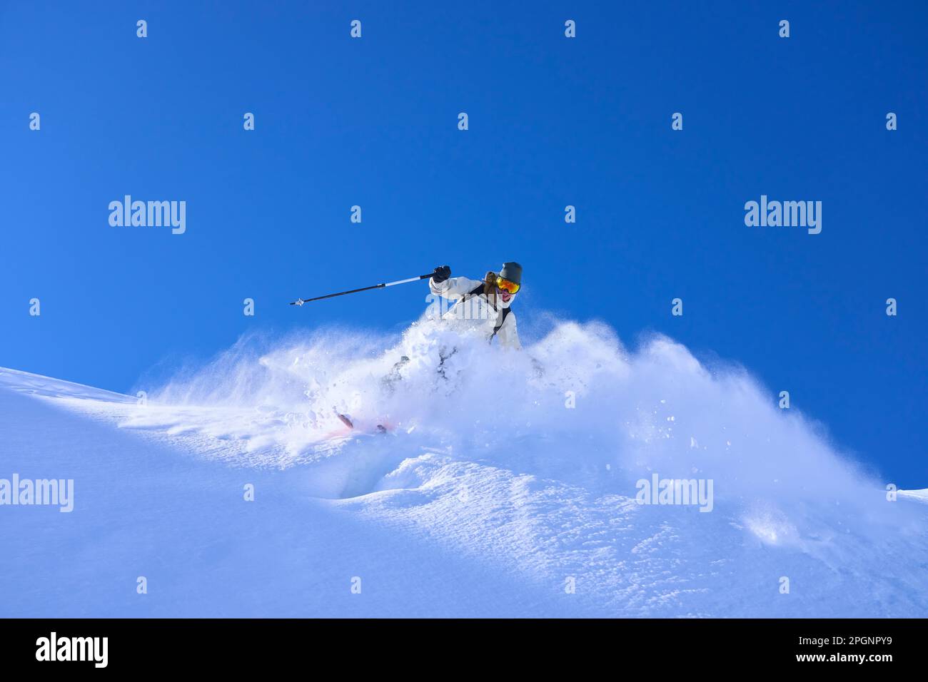 Mature woman skiing downhill under blue sky Stock Photo