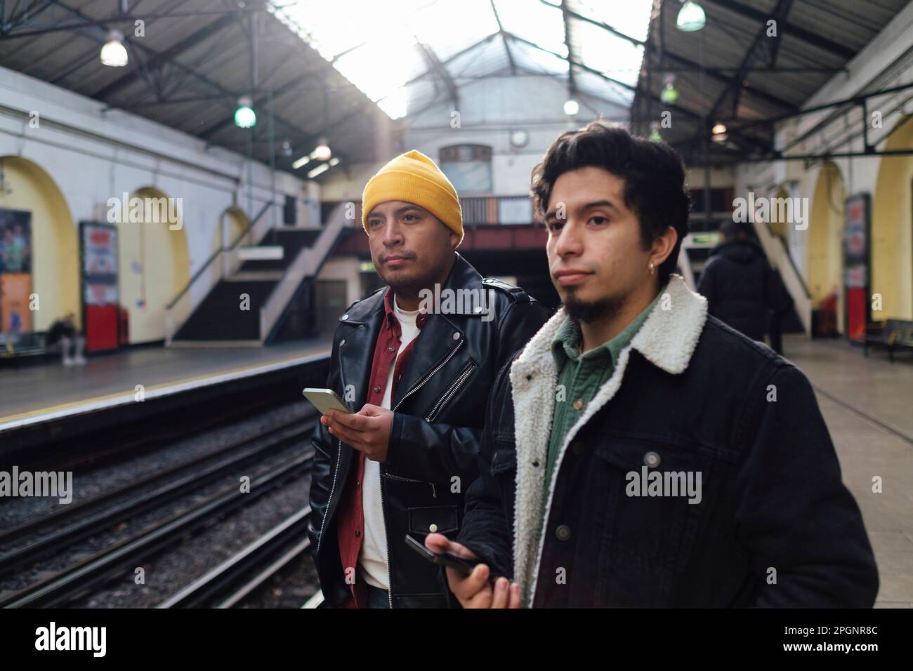 Brothers holding smart phones standing at railroad station platform Stock Photo