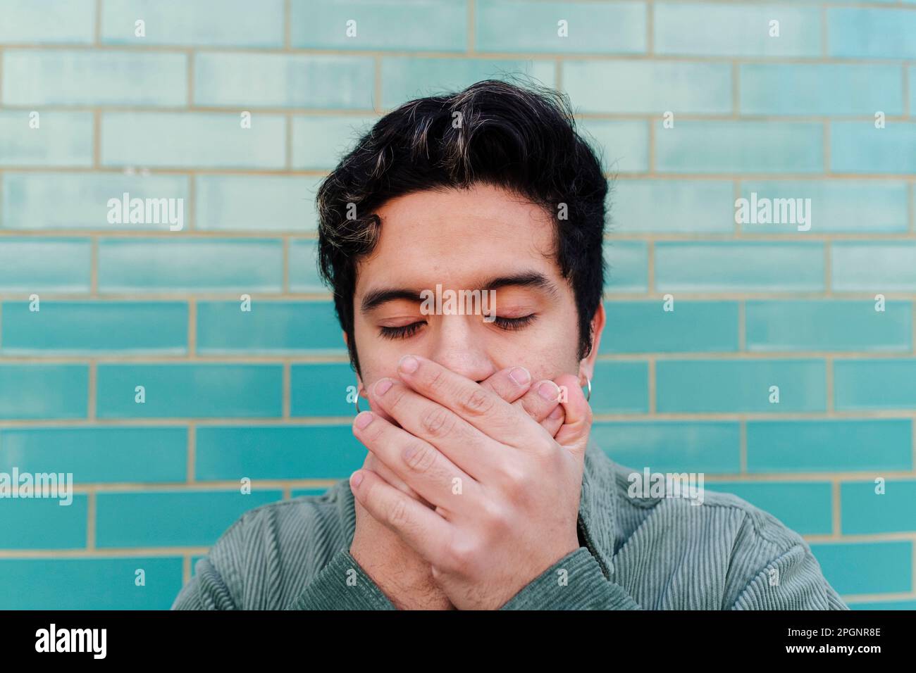 Young man covering mouth with hands in front of brick wall Stock Photo