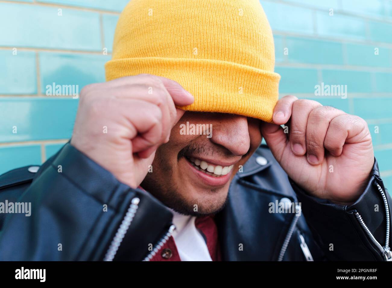 Smiling man covering face with yellow knit hat Stock Photo
