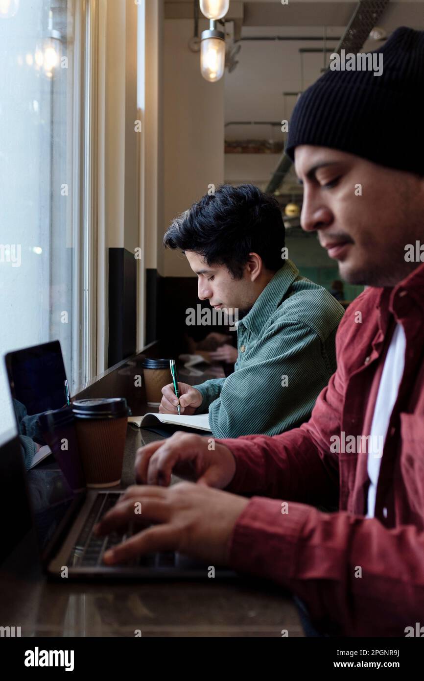 Freelancer working on laptop with brother in cafe Stock Photo