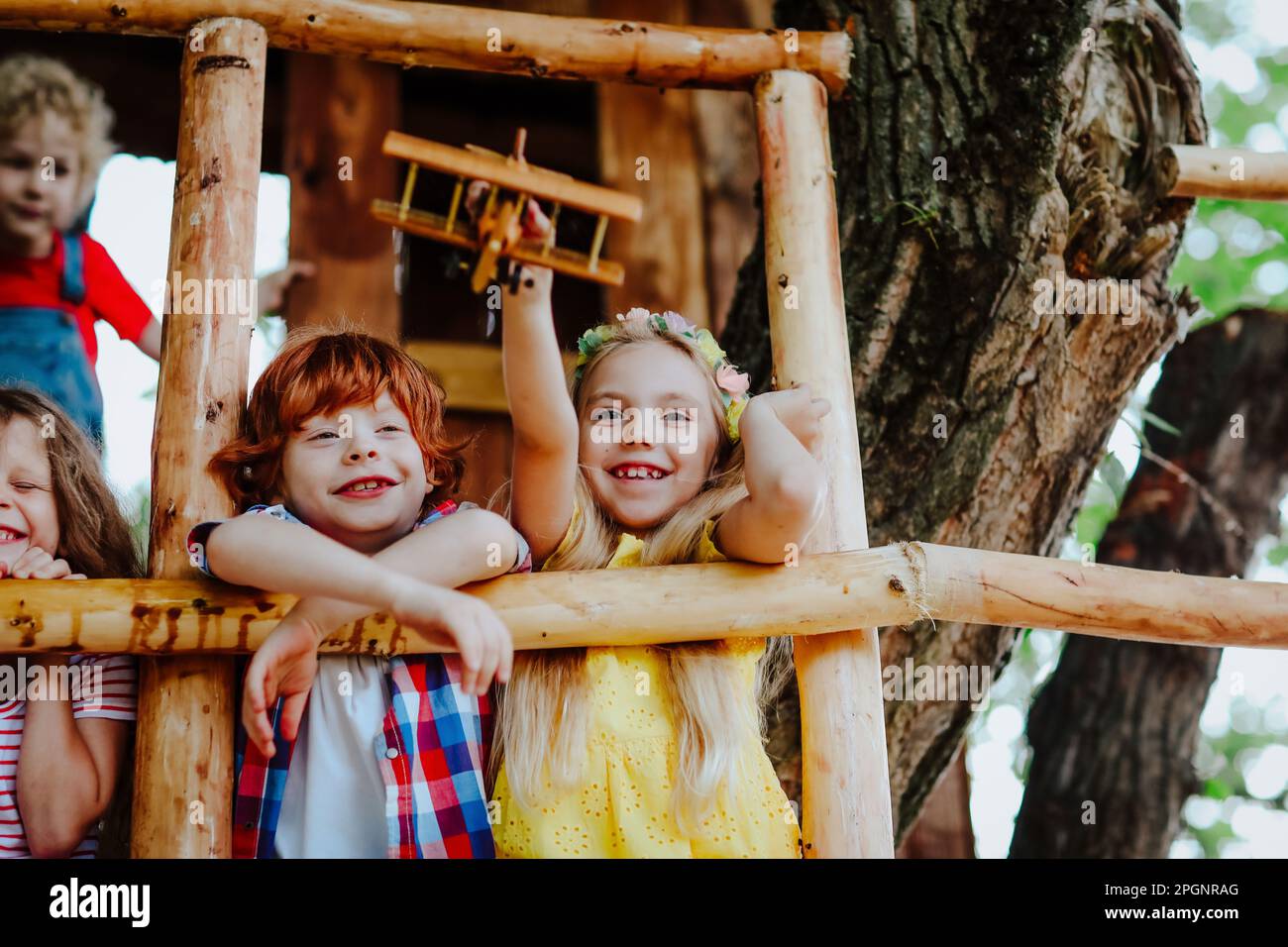 Smiling girl playing with toy airplane by friends on tree house Stock Photo